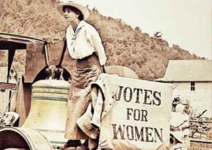 image of woman standing beside the women's Justice Bell and a sign saying Votes for Women