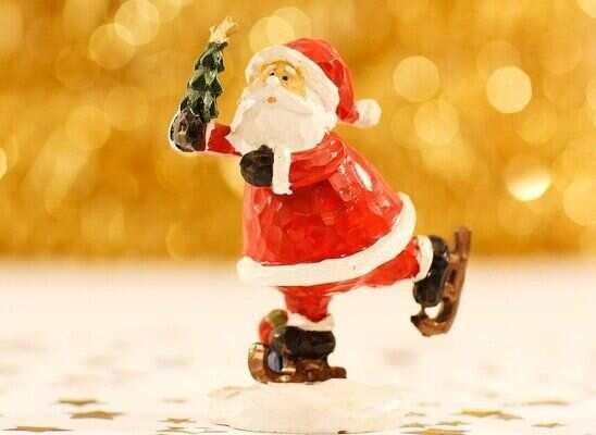 Photo of Santa Claus ice skating while holding a miniature Christmas tree.